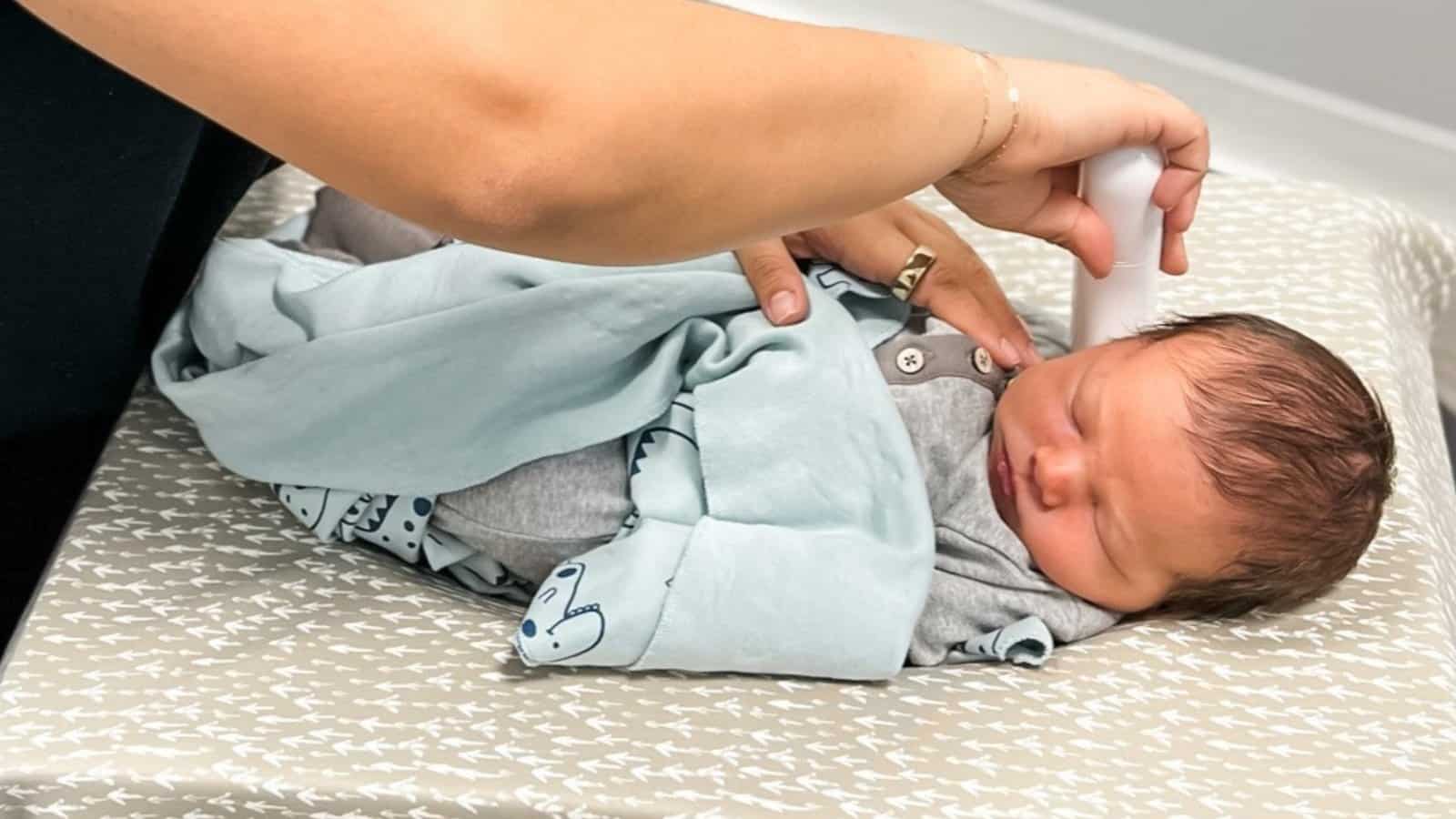 Birth Trauma in Babies featured image A sleeping newborn wrapped in a soft blue blanket gets a gentle nervous system scan at Perfect by Design